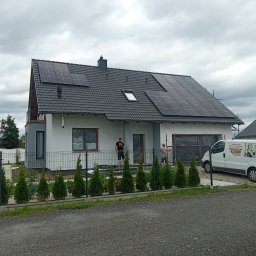 G.M Complex -Profi - Nowoczesny dom z panelami słonecznymi na dachu, widoczny zza ogrodzenia, z ekipą montującą i zaparkowanym busem firmy. Pochmurne niebo w tle.