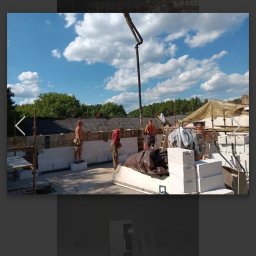 G.M Complex -Profi - Murowanie ścian z betonu komórkowego na budowie domu jednorodzinnego. Na pierwszym planie murarze przy pracy, w tle pompa do betonu i błękitne niebo.