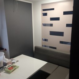 G.M Complex -Profi - Nowoczesne wnętrze jadalni z szarą ścianą, białym stołem i zabudowaną ławą. Dekoracyjny panel ścienny z poziomymi wycięciami. Minimalistyczny design, jasne oświetlenie.