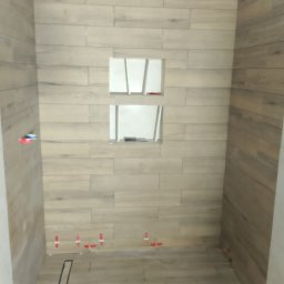 G.M Complex -Profi - Wykończona kabina prysznicowa z drewnopodobnymi płytkami, wnękami i odpływem liniowym. Widoczne elementy poziomowania płytek.