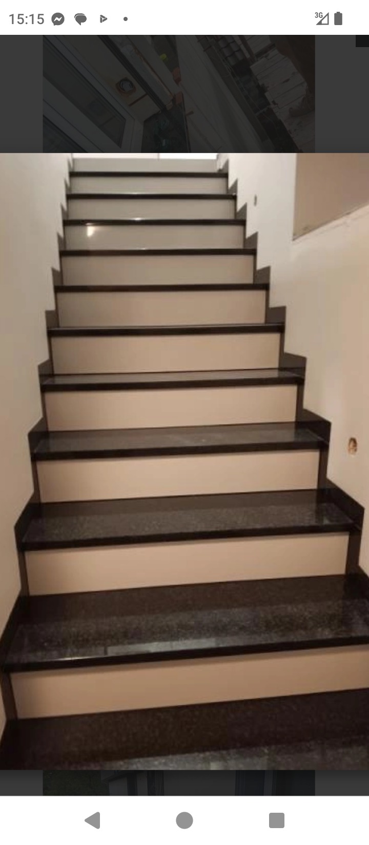 Schody wewnętrzne z ciemnego kamienia i jasnych podstopnic, widok z dołu. Ściany białe, minimalistyczny design.