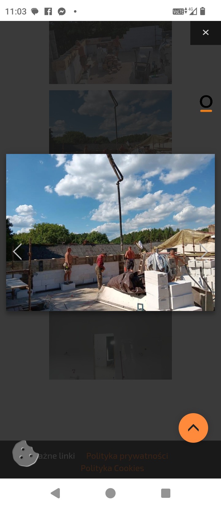 Murowanie ścian z betonu komórkowego na budowie domu jednorodzinnego. Na pierwszym planie murarze przy pracy, w tle pompa do betonu i błękitne niebo.