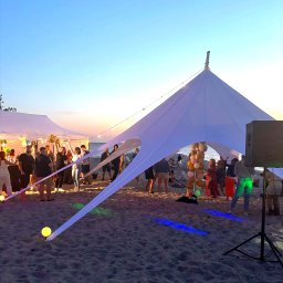 3Life - Plażowa impreza pod białym namiotem w kształcie gwiazdy, oświetlonym kolorowymi światłami. W tle zachód słońca i bawiący się ludzie.