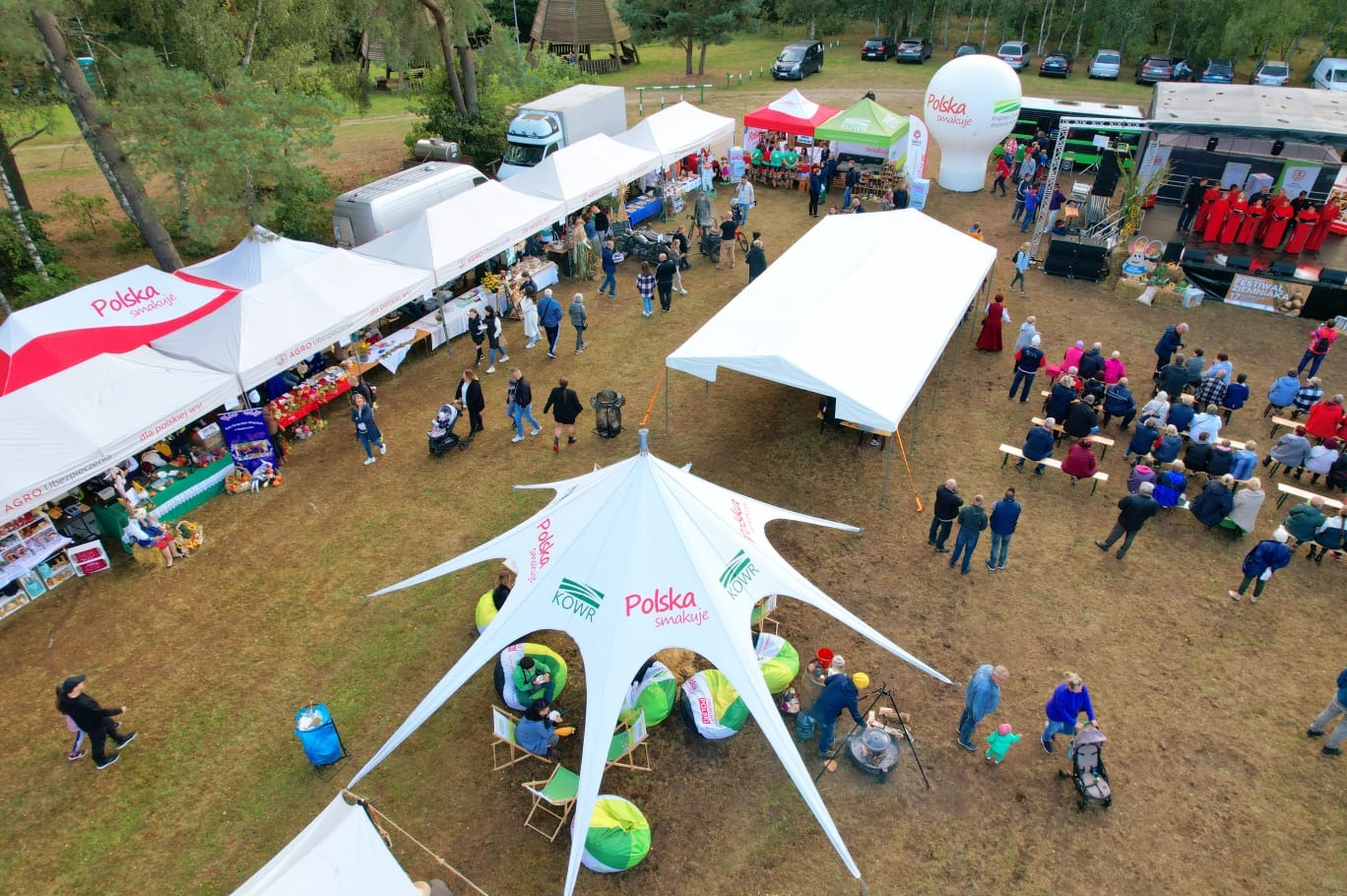 Widok z góry na plenerowy festyn z białymi namiotami, sceną i publicznością. Centralnie namiot gwiazda z logo 'Polska smakuje'.