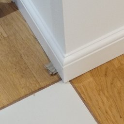 Marcin Polek Usługi Remontowo-Serwisowe MM - Świeżo pomalowany narożnik ściany z białą listwą przypodłogową, częściowo przykryty folią malarską na drewnianej podłodze.