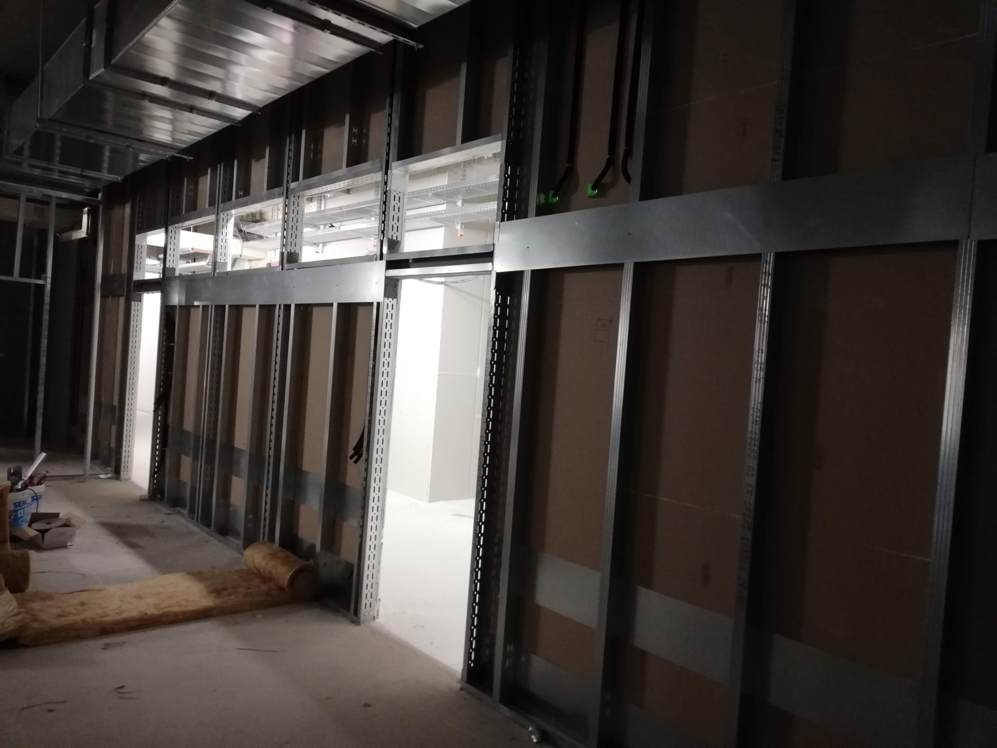 Konstrukcja szkieletowa z profili metalowych i płyt kartonowo-gipsowych w trakcie montażu, widoczna izolacja z wełny mineralnej na podłodze, wentylacja pod sufitem.