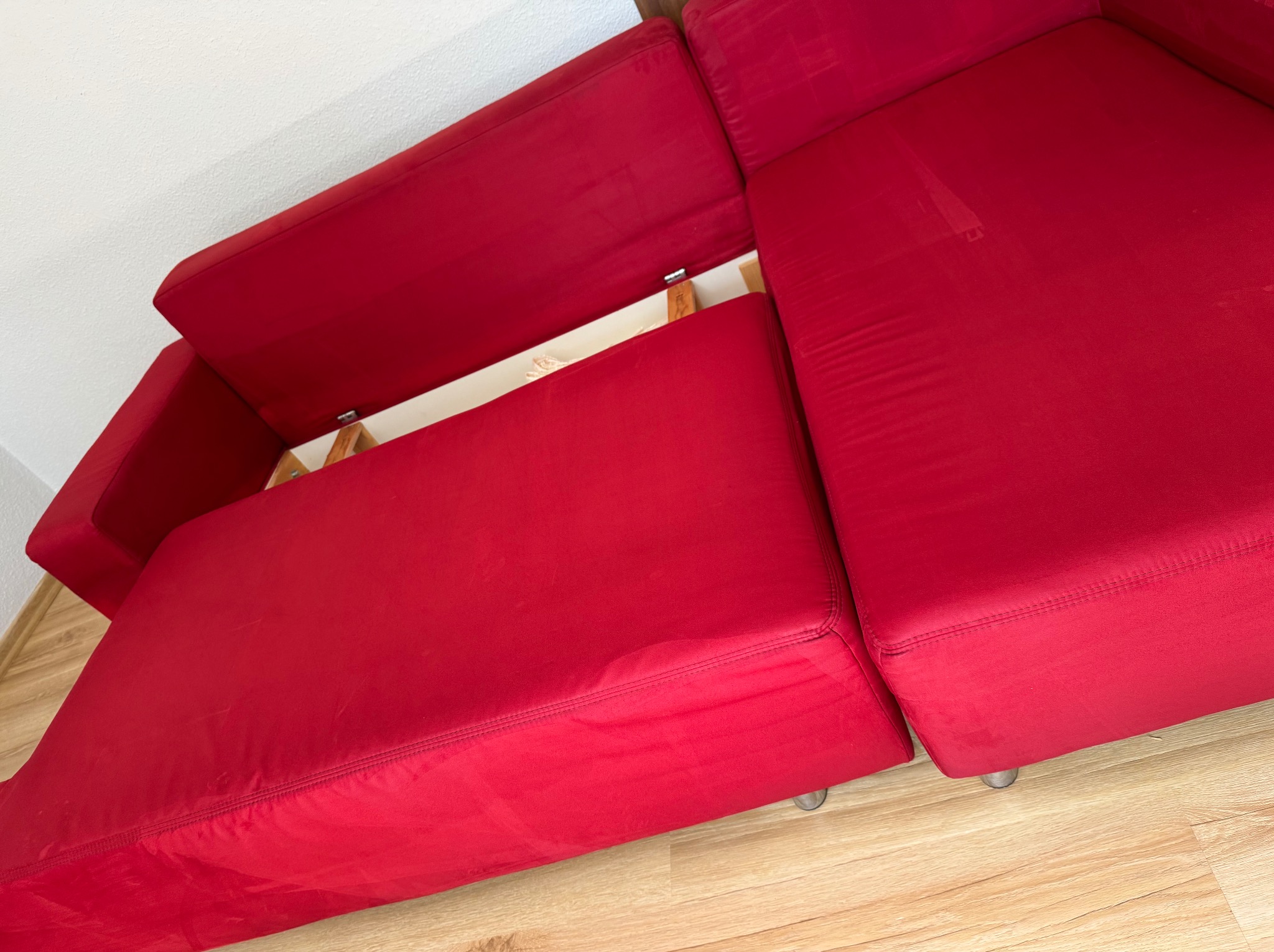 Czerwona rozkładana sofa z widocznym mechanizmem, częściowo rozłożona na drewnianej podłodze. Widoczne ślady użytkowania na siedzisku.