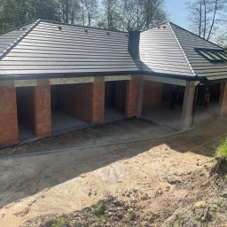 R&S DOORS SPÓŁKA Z OGRANICZONĄ ODPOWIEDZIALNOŚCIĄ - Surowy stan budynku z cegły z szarym dachem i oknami dachowymi, widoczne przygotowania do montażu, teren wokół w stanie roboczym, błoto.