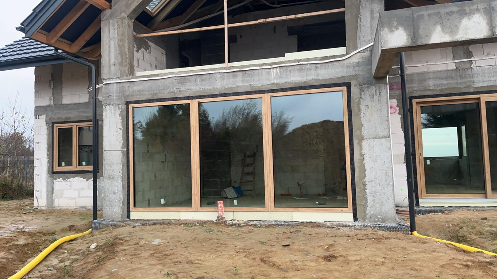 Montaż okien w surowym stanie domu z bloczków, widoczne drewniane ramy okienne i drabina oparta o ścianę wewnątrz budynku.