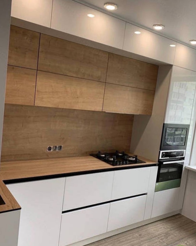 Nowoczesna kuchnia z białymi szafkami dolnymi i drewnianymi górnymi, oświetleniem LED i czarnym blatem. Widoczna płyta gazowa i piekarnik w zabudowie.