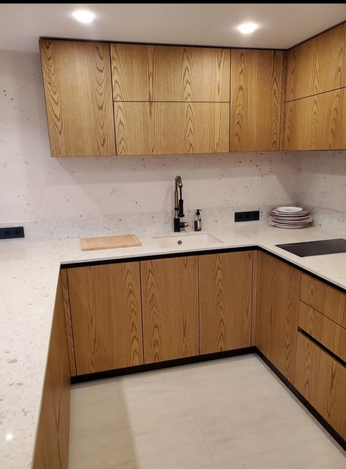 Jasna kuchnia na wymiar z drewnianymi frontami i czarnymi akcentami. Blat z białego kamienia, nowoczesna armatura, minimalistyczny design.