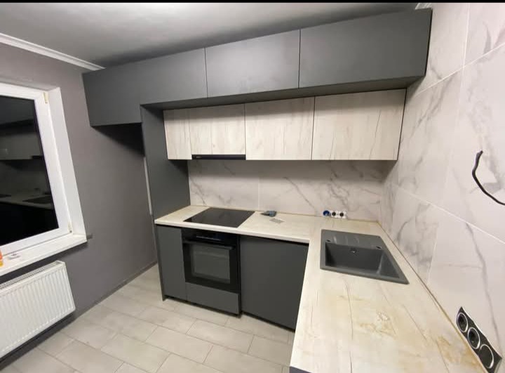 Nowoczesna kuchnia z szarymi szafkami górnymi i dolnymi, blatem imitującym drewno oraz marmurowymi płytkami na ścianie. Widoczny piekarnik i płyta indukcyjna.