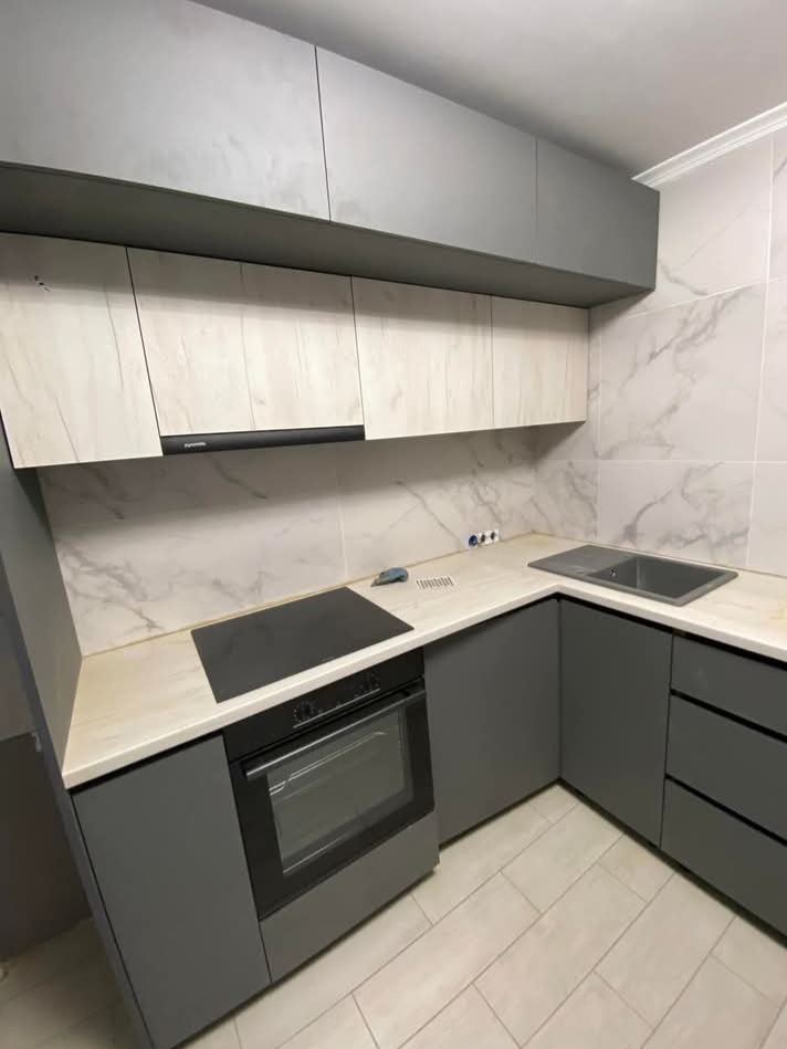 Nowoczesna kuchnia na wymiar z szarymi, matowymi frontami i marmurowym blatem. Widoczna płyta indukcyjna i piekarnik w zabudowie. Uwagę zwracają górne szafki w dwóch odcieniach.