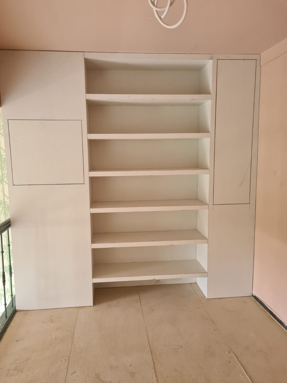 Wnęka z półkami, świeżo pomalowana na biało, z widocznymi śladami niedawnych prac wykończeniowych na podłodze i ścianach.