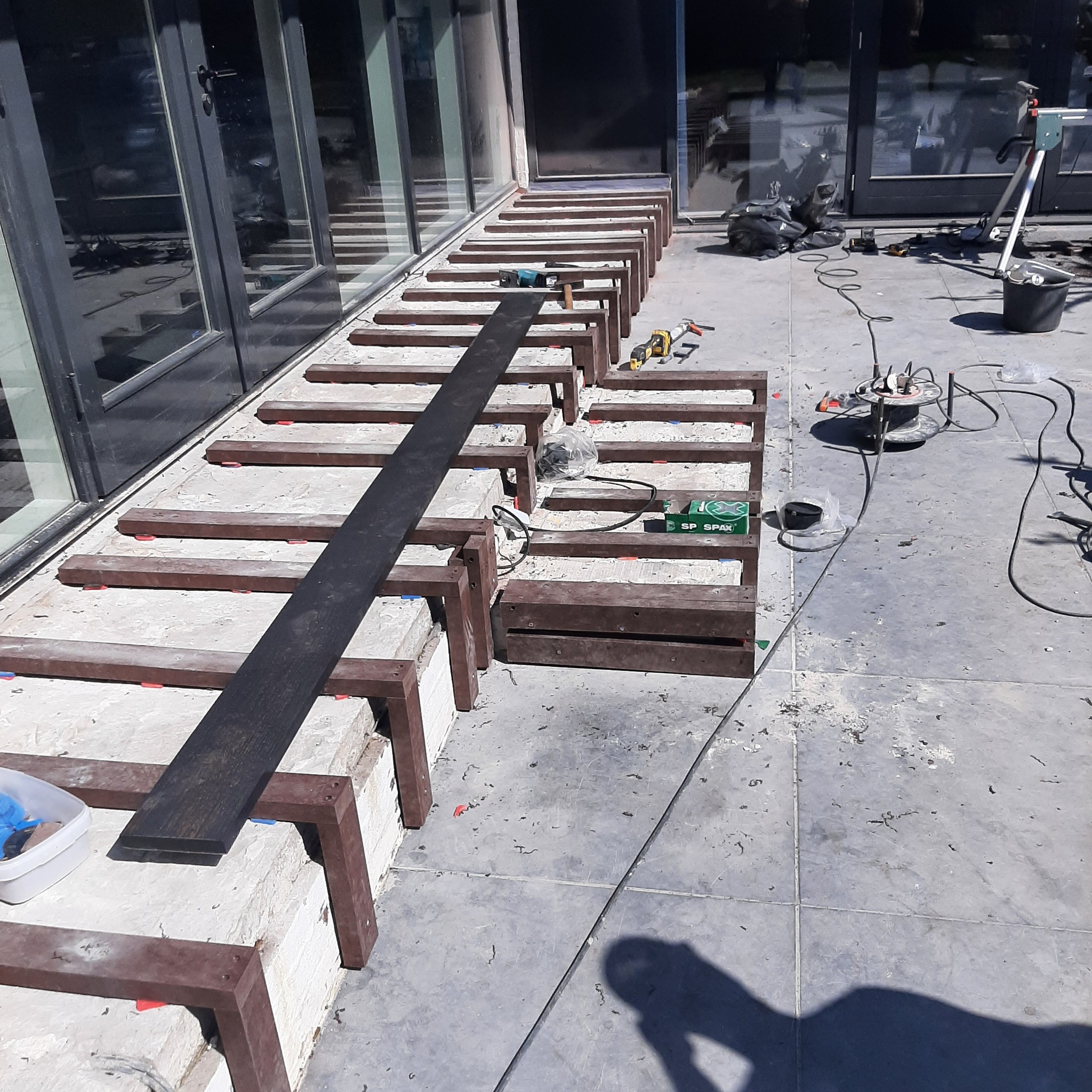 Konstrukcja pod taras z legarów kompozytowych na regulowanych wspornikach, widoczne narzędzia i materiały budowlane.