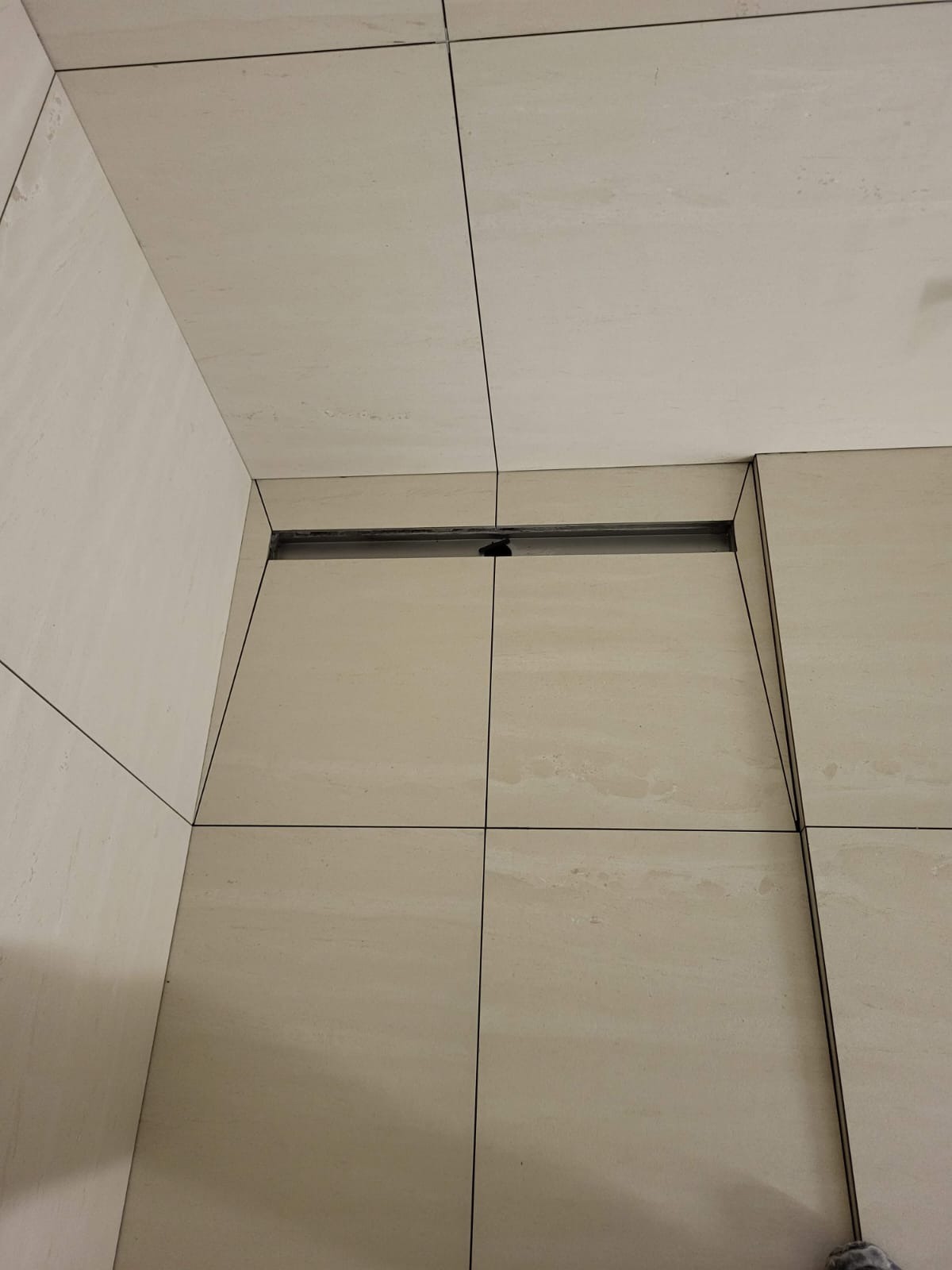 Beżowe płytki podłogowe i ścienne w łazience, z widocznym liniowym odpływem podłogowym, zamontowanym przy ścianie.