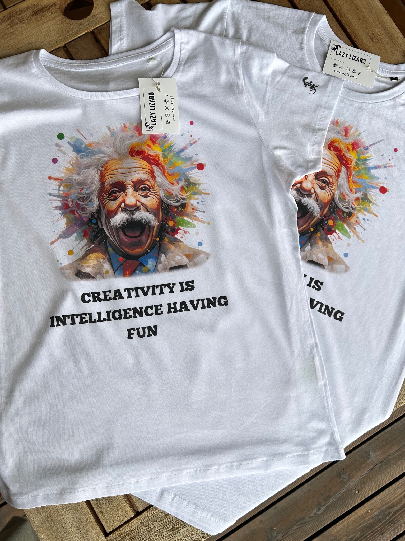 Białe koszulki z nadrukiem Alberta Einsteina i hasłem w Wielkiej Wsi. Widoczny metka marki Lazy Lizard.
