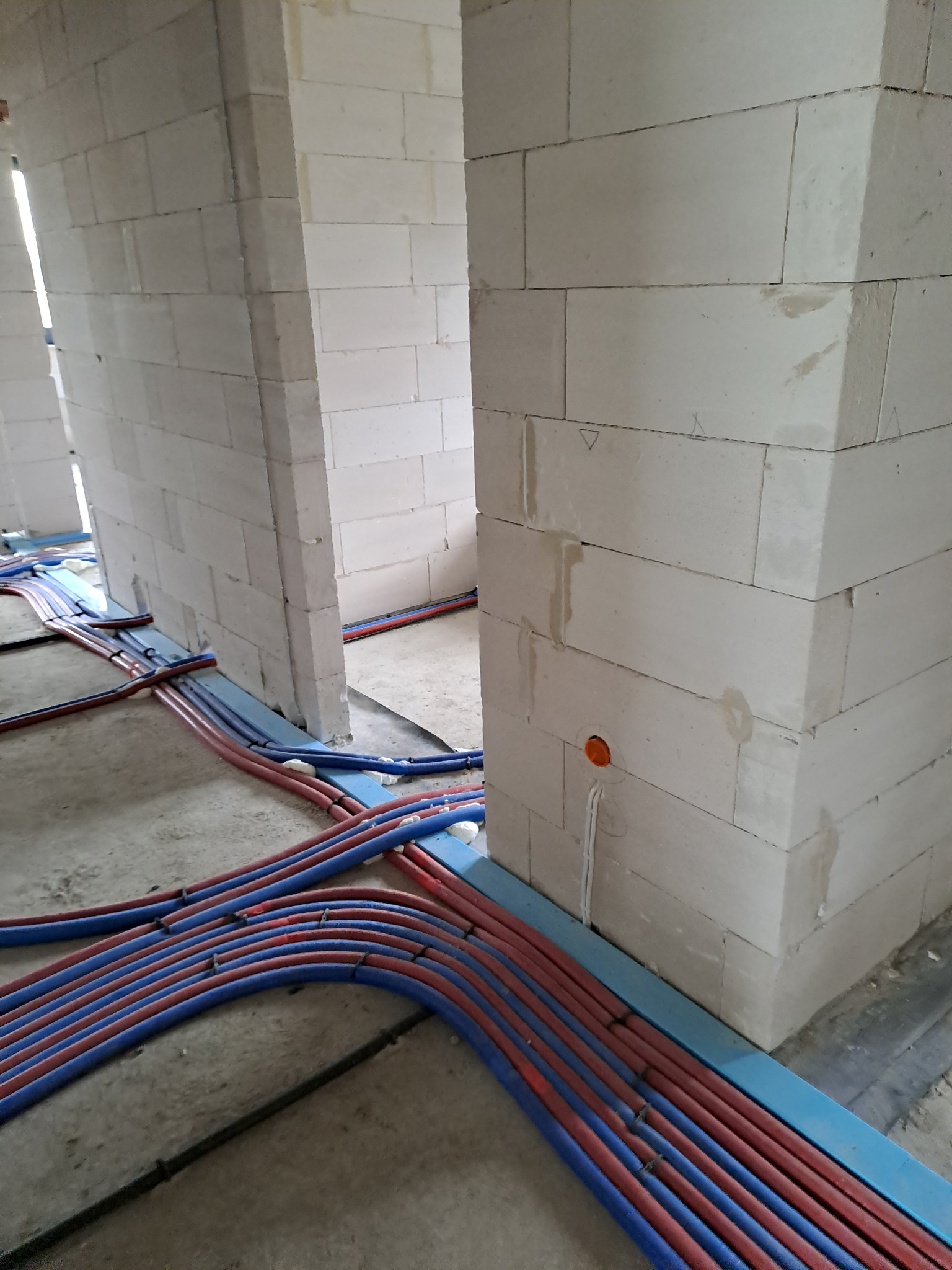 Wnętrze w trakcie budowy z widocznymi przewodami elektrycznymi w peszlach ułożonymi wzdłuż ściany z betonu komórkowego, z widocznym gniazdkiem podtynkowym.