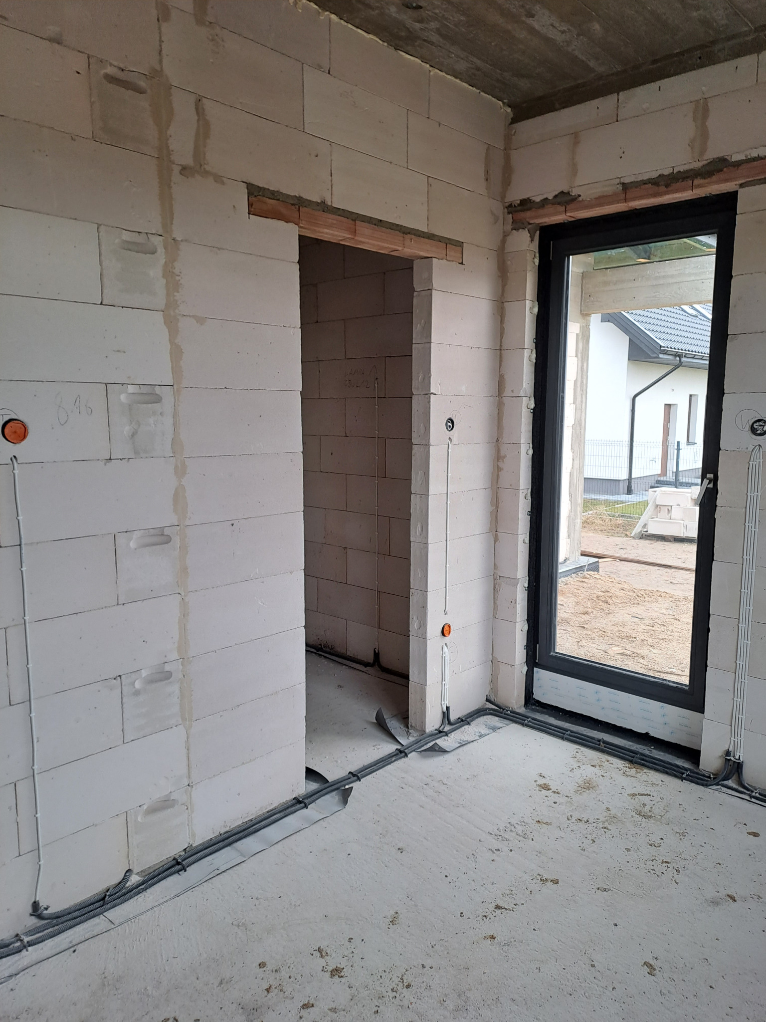 Surowy stan: widok wnętrza budynku w trakcie budowy z widocznymi przewodami elektrycznymi ułożonymi wzdłuż ścian z betonu komórkowego, puszki instalacyjne w ścianach, przygotowane otwory okienne...