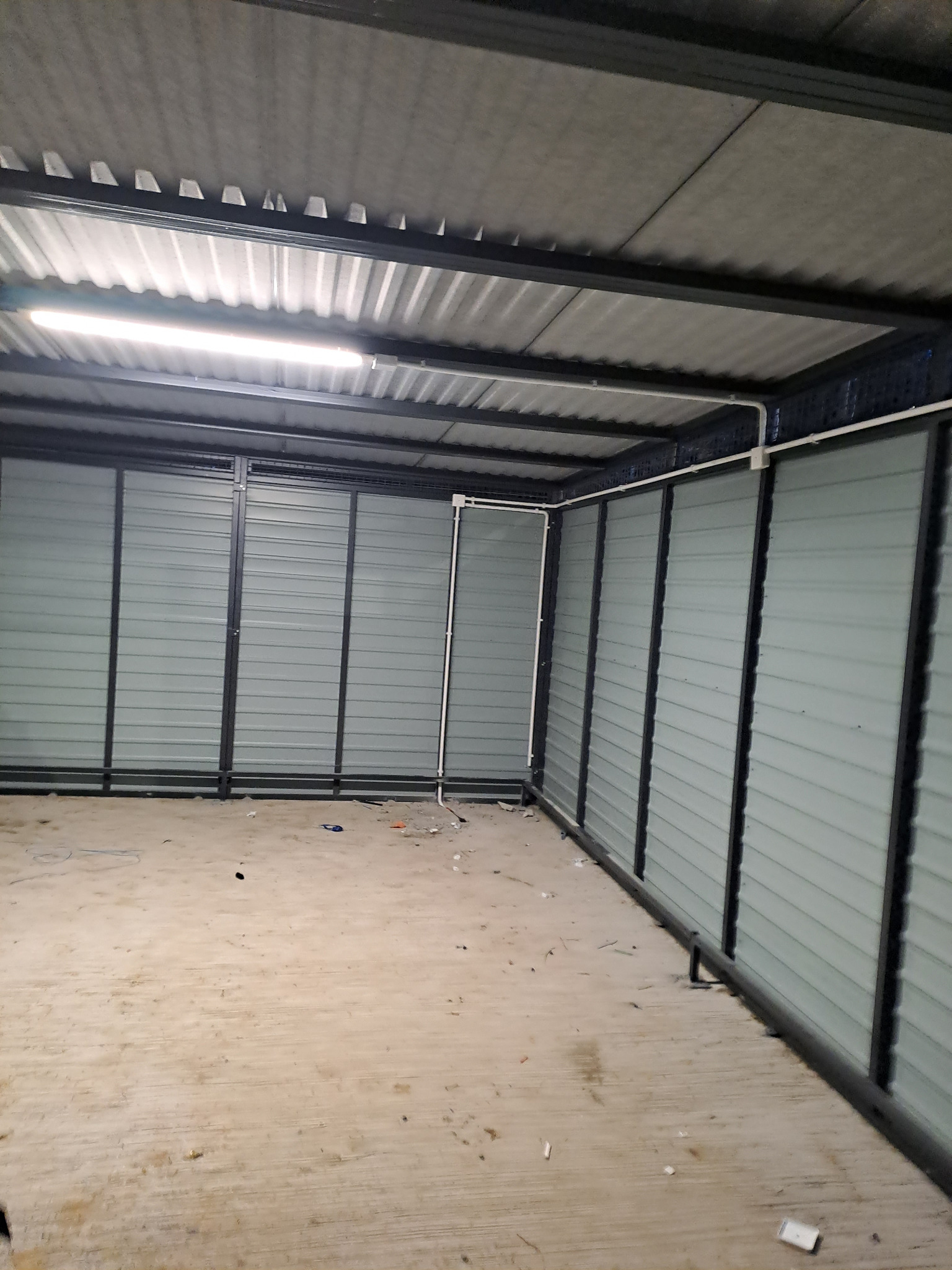 Wnętrze hali magazynowej z zamontowanym oświetleniem liniowym LED, widoczne szare ściany z blachy trapezowej i betonowa posadzka w stanie surowym.