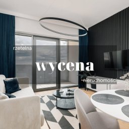 Madro Real Estate Szczecin - Kreatywna sprzedaż nieruchomości - Pas nadmorski - Nowoczesny salon z balkonem, szarą sofą z poduszkami, okrągłym stolikiem kawowym, dywanem w geometryczne wzory i czarną ścianą z telewizorem. Okrągła lampa sufitowa i widok na miasto z balkonu.