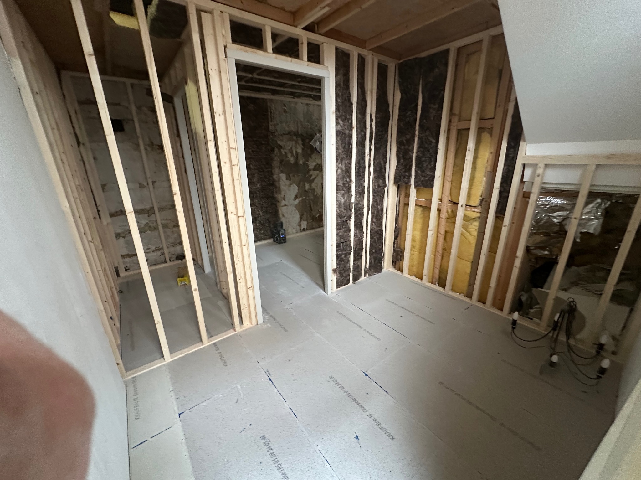 Wnętrze w trakcie budowy: drewniana konstrukcja ścian działowych z izolacją z wełny mineralnej, podłoga wyłożona płytami izolacyjnymi, widoczne przewody elektryczne i fragment ściany z surową cegłą...