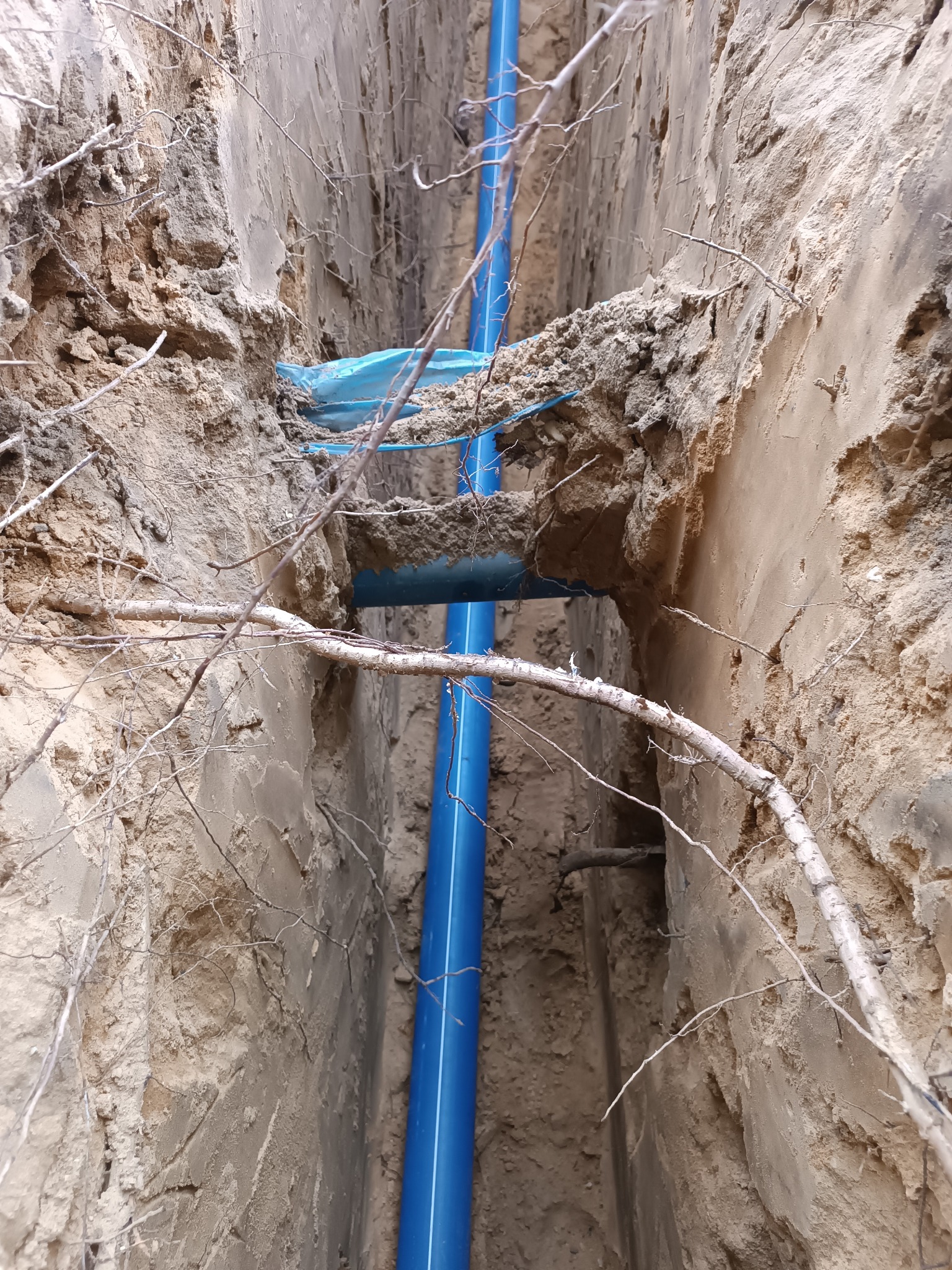 Niebieska rura w wykopie ziemnym, zabezpieczona folią, widok z góry. Prace instalacyjne w Siemiatyczach. Wykop pod instalacje sanitarne.