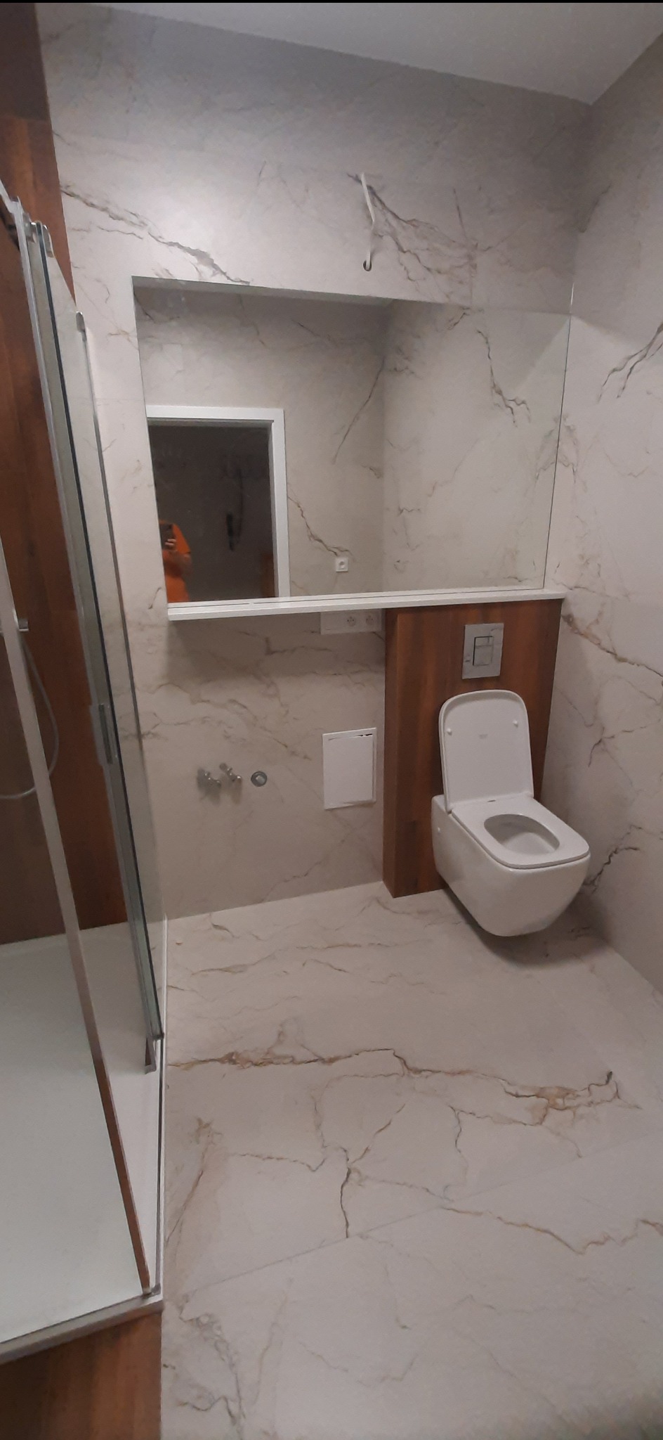 Nowoczesna łazienka z kabiną prysznicową, toaletą podwieszaną i lustrem, wykończona płytkami imitującymi marmur.