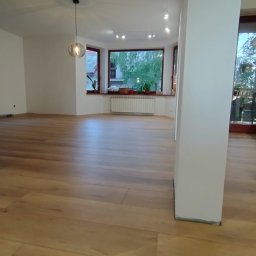 NEOWNĘTRZE SPÓŁKA Z OGRANICZONĄ ODPOWIEDZIALNOŚCIĄ - Jasna, drewniana podłoga w przestronnym salonie z dużym oknem wykuszowym i widokiem na zieleń, z kolumną w centrum kadru i wiszącą lampą.