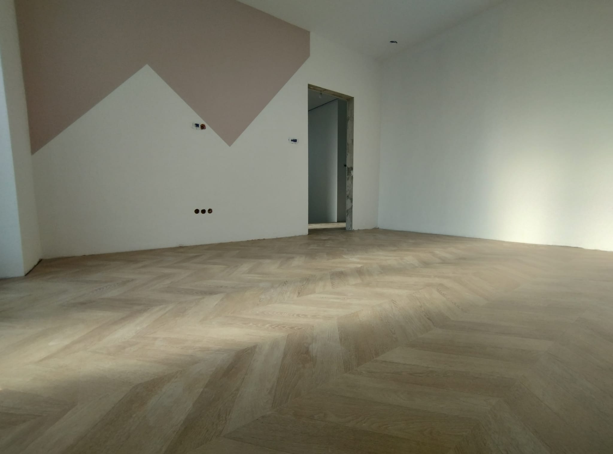 Ukończona podłoga ułożona w jodełkę francuską w pustym pokoju z pomalowaną ścianą w geometryczne wzory.