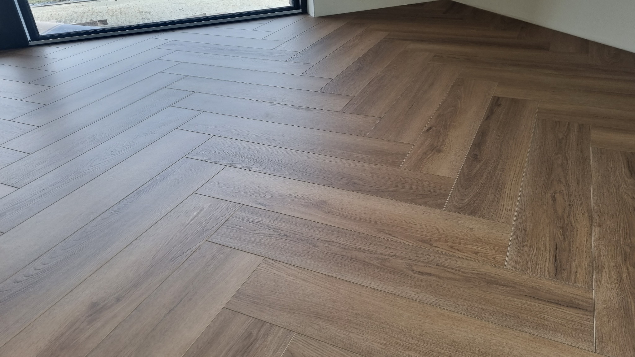 Ułożona podłoga z paneli w jodełkę, widok z góry, naturalne oświetlenie z okna.