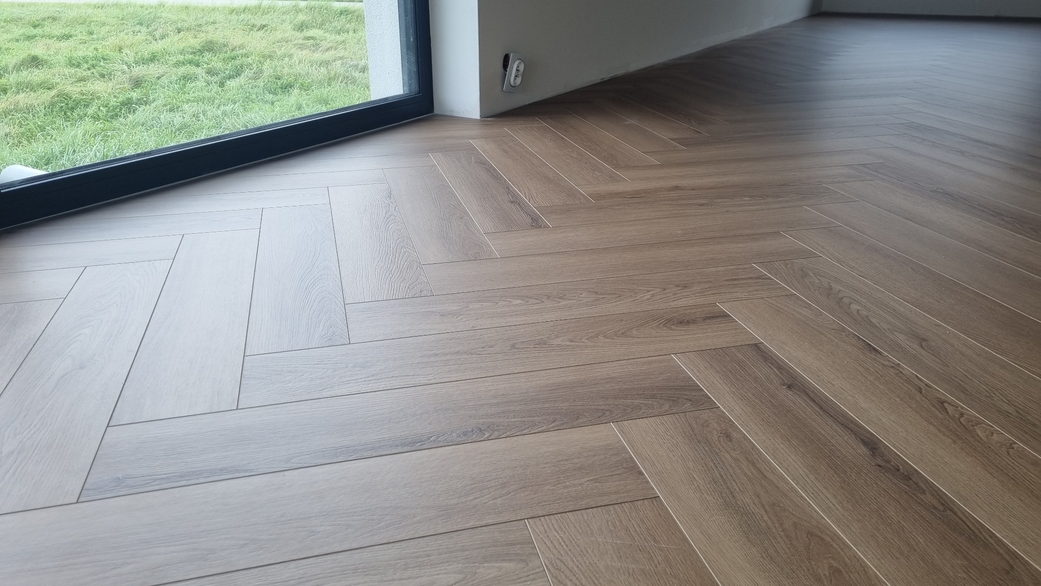 Ułożona podłoga z paneli w jodełkę, widok z góry, przy oknie z widokiem na zieleń.