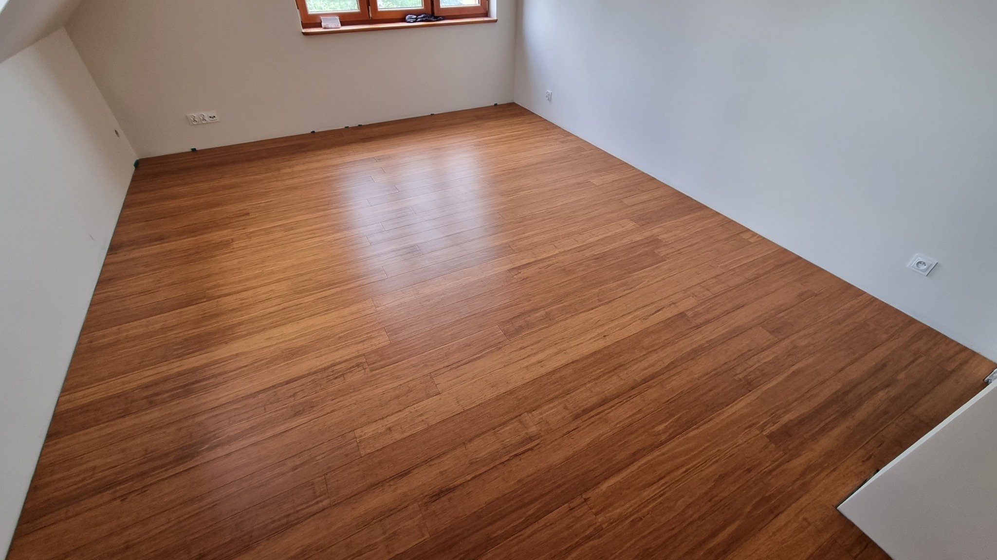 Ułożone panele podłogowe w jasnym pomieszczeniu z widocznym oknem i listwami przypodłogowymi w trakcie montażu.