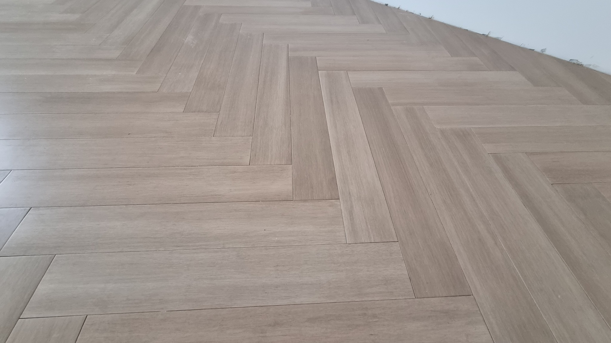 Ułożone jasne panele podłogowe w jodełkę, widoczny fragment białej ściany w rogu.