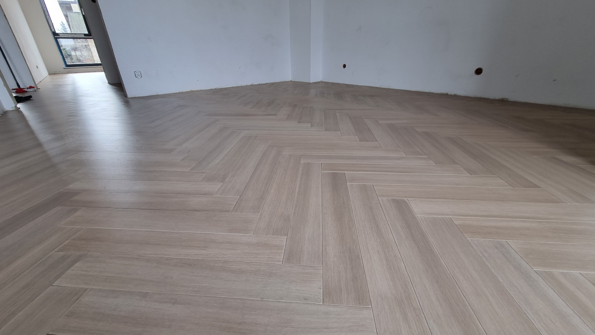Ułożona podłoga z paneli w jodełkę, widoczne białe ściany i okno w tle.