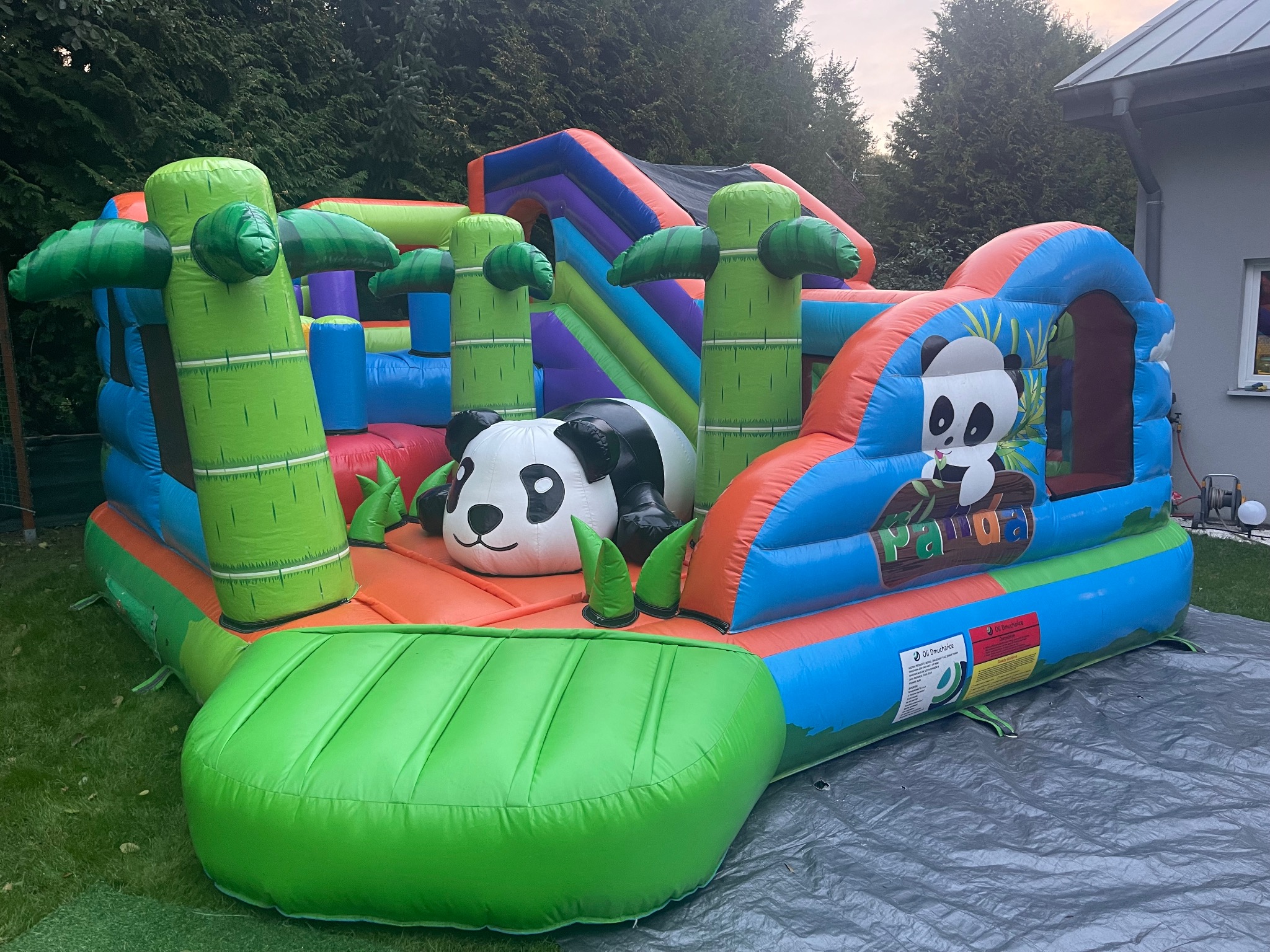 Kolorowy dmuchany plac zabaw z motywem pandy i bambusów, ustawiony na trawie. Widoczne elementy do skakania i zjeżdżania. Idealny na imprezy plenerowe dla dzieci.