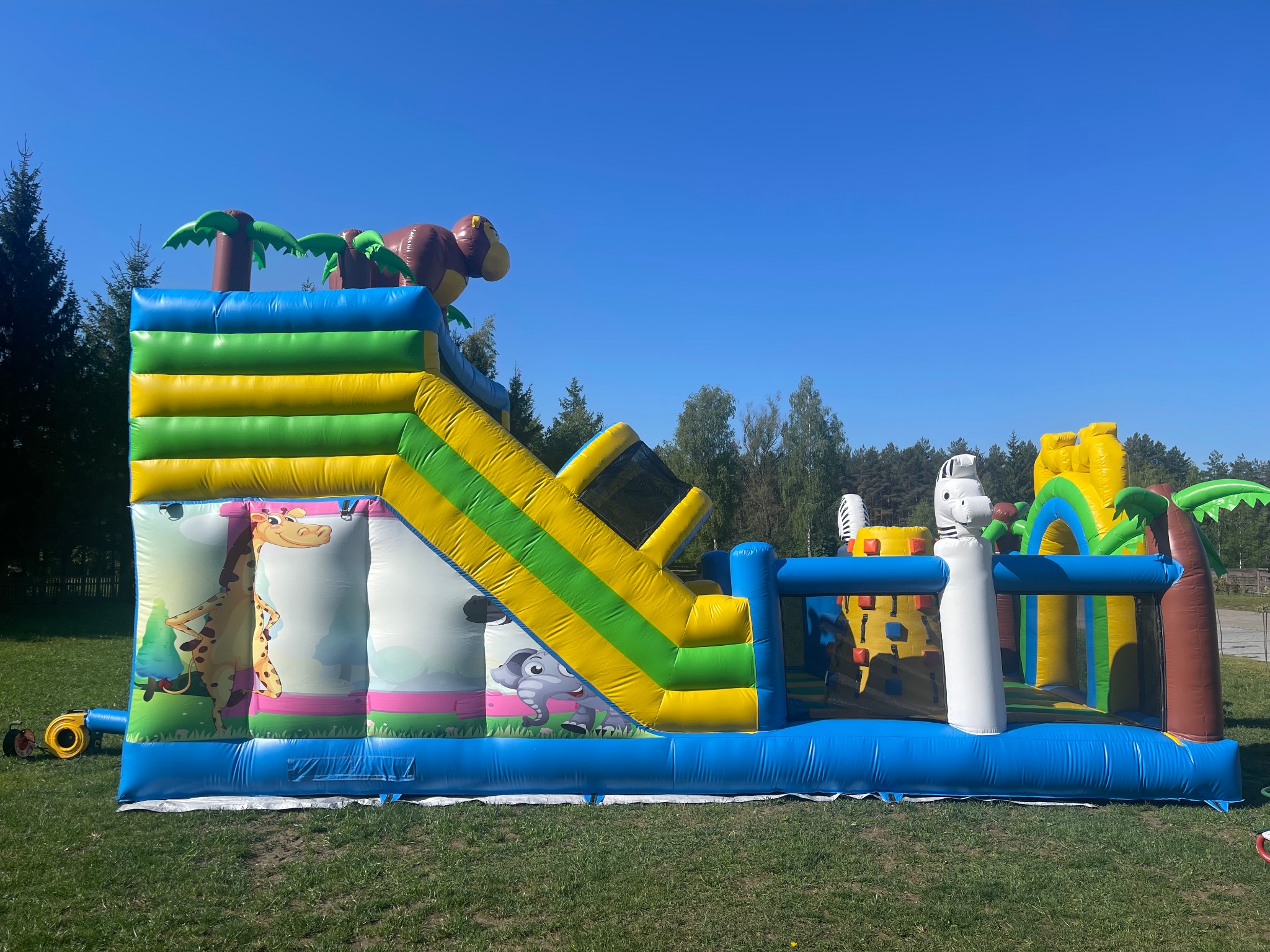 Kolorowy dmuchany plac zabaw z motywem dżungli, zjeżdżalnią i palmami, rozstawiony na trawie w Białymstoku. Idealny na imprezy plenerowe dla dzieci.