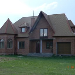 Mirosław JOŃCA MJ PROJECT - Dwukondygnacyjny dom z czerwonej cegły z brązowym dachem z blachy falistej, widok z przodu na trawnik.