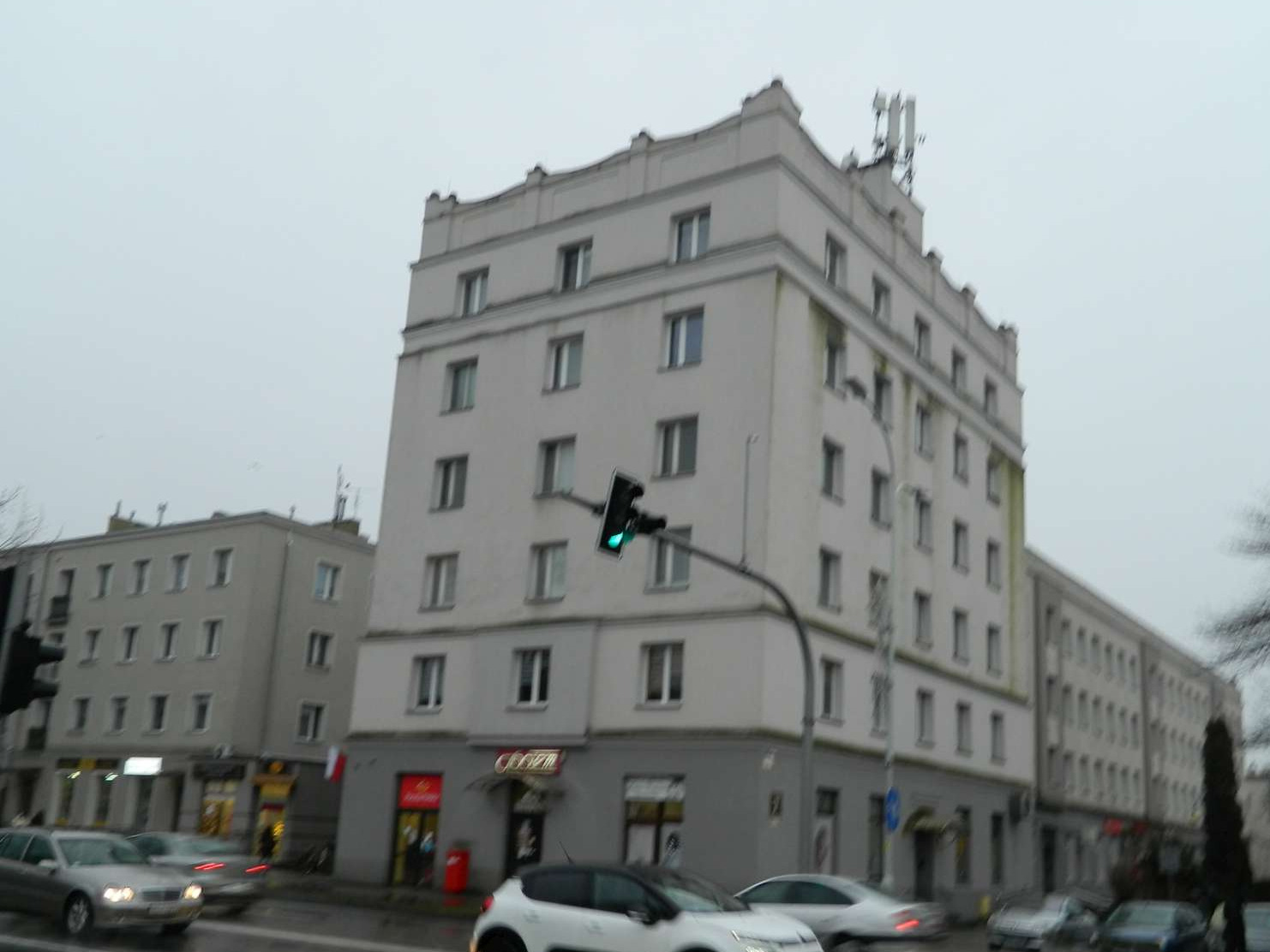 Biurowiec z antenami na dachu, widziany z ulicy w pochmurny dzień.