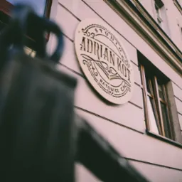 Elewacja budynku z szyldem studia 'Adrian Kot' w Katowicach, widoczne okno i fragment balustrady.