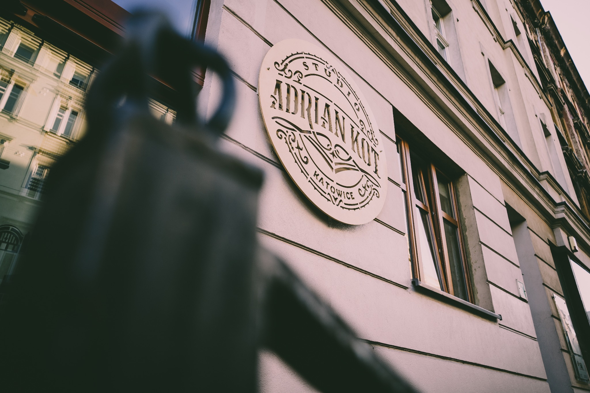 Elewacja budynku z szyldem studia 'Adrian Kot' w Katowicach, widoczne okno i fragment balustrady.