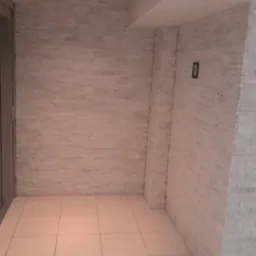 Wnętrze po remoncie: ściany wyłożone jasną, dekoracyjną cegłą, podłoga z jasnych, kwadratowych płytek, oświetlenie sufitowe punktowe, widoczny fragment drzwi po lewej stronie i mały numer '0'...