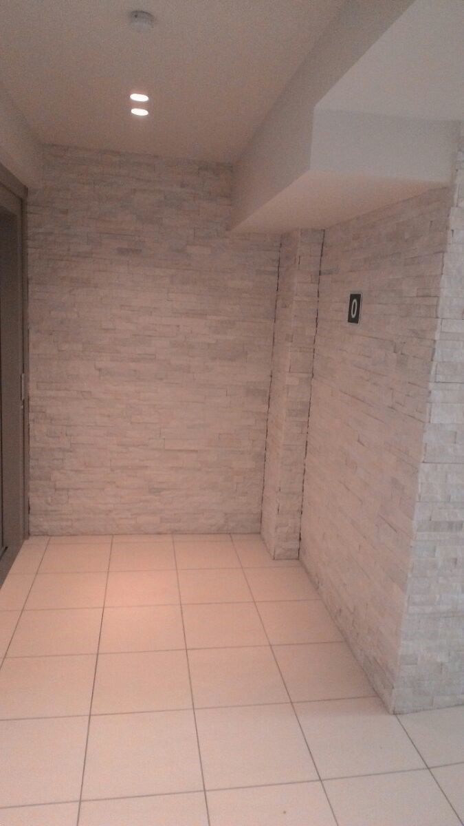 Wnętrze po remoncie: ściany wyłożone jasną, dekoracyjną cegłą, podłoga z jasnych, kwadratowych płytek, oświetlenie sufitowe punktowe, widoczny fragment drzwi po lewej stronie i mały numer '0'...