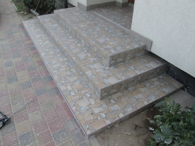 Wykończone płytkami schody wejściowe do budynku z widocznym fragmentem chodnika z kostki brukowej i narzędziem do fugowania.