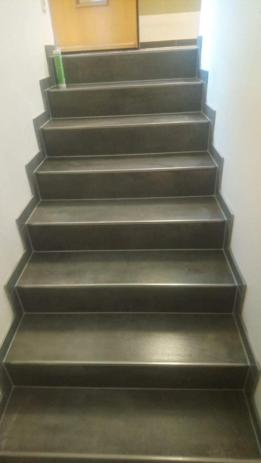 Wykończone schody wewnętrzne z ciemnoszarej płyty, widok z dołu, z widoczną tubą kleju na górnym stopniu.