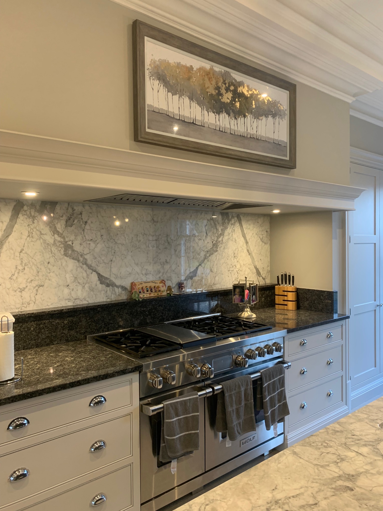 Elegancka kuchnia z marmurowym backsplash'em, granitowym blatem i profesjonalną kuchenką Wolf z trzema ręcznikami.