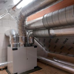 Firma Handlowo-Usługowa Krzysztof Ścibior - Centrala wentylacyjna z izolowanymi przewodami w pomieszczeniu z wykończeniem z płyty OSB i izolacją, widoczne rury wentylacyjne z folią aluminiową.