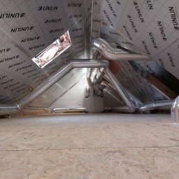 Firma Handlowo-Usługowa Krzysztof Ścibior - Instalacja rekuperacji na poddaszu z widocznymi rurami wentylacyjnymi, centralą i izolacją Unilin na skośnym dachu.