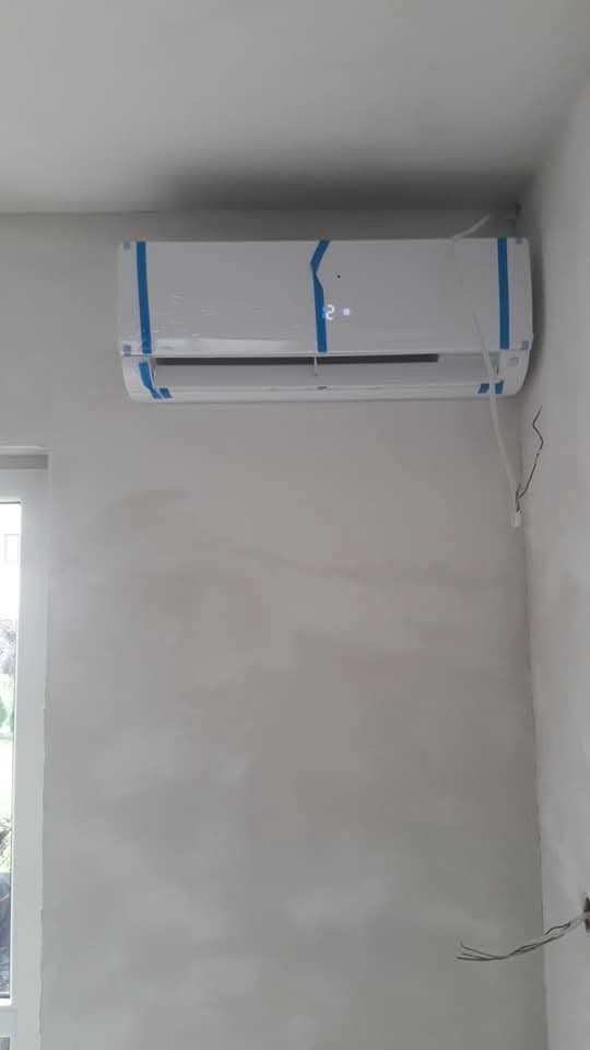 Nowo zamontowana, biała klimatyzacja ścienna w surowym wnętrzu, zabezpieczona niebieską taśmą, widoczne wystające kable elektryczne