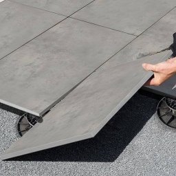 WAWER-BRUK Mariusz Wiącek - Montaż tarasu wentylowanego z płyt betonowych na regulowanych wspornikach, widoczne podłoże żwirowe i fragment buta montera.